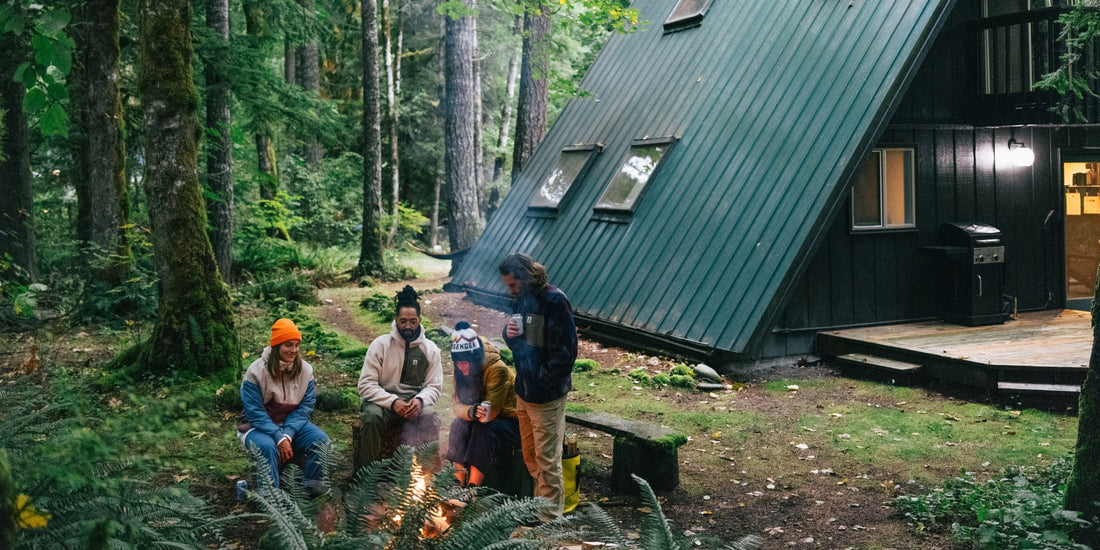 A group of friends hang around a campfire outside a cabin in the woods