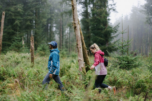 A man and a woman walk through a forest wearing waterproof jackets