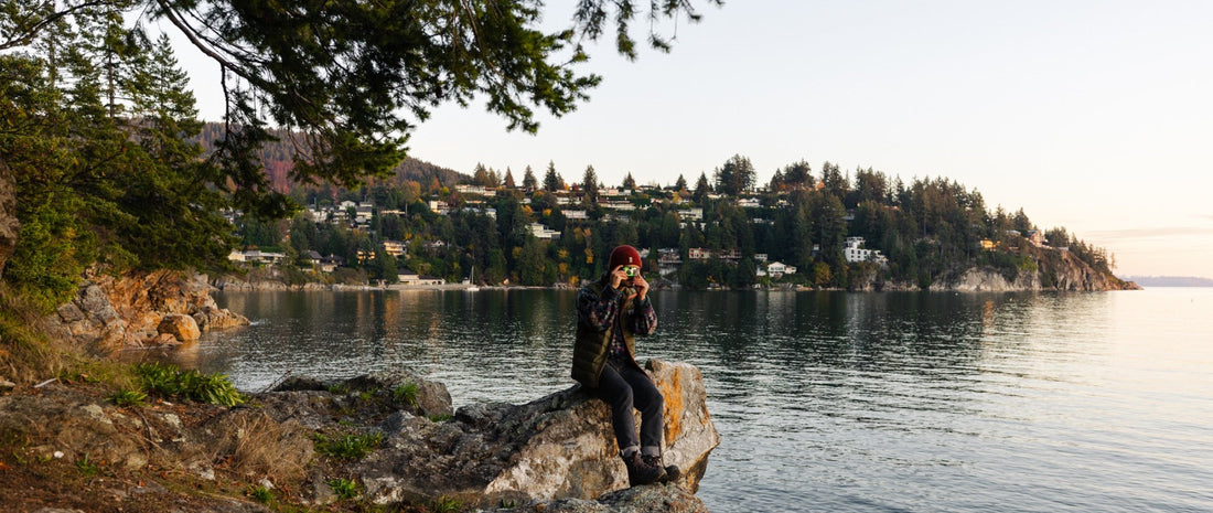 A man sitting by the side of a lake in Vancouver, holding a disposable camera